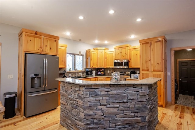 kitchen featuring appliances with stainless steel finishes, light brown cabinets, a sink, light stone countertops, and light wood-type flooring