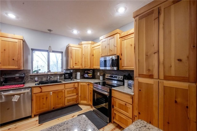 kitchen featuring light stone counters, stainless steel appliances, a sink, hanging light fixtures, and backsplash