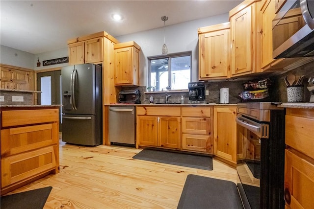 kitchen with light wood-style flooring, stainless steel appliances, a sink, backsplash, and decorative light fixtures