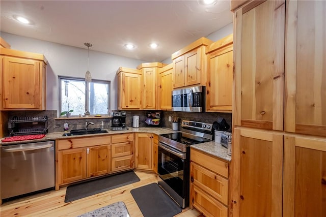 kitchen featuring light stone counters, light wood finished floors, stainless steel appliances, decorative backsplash, and a sink