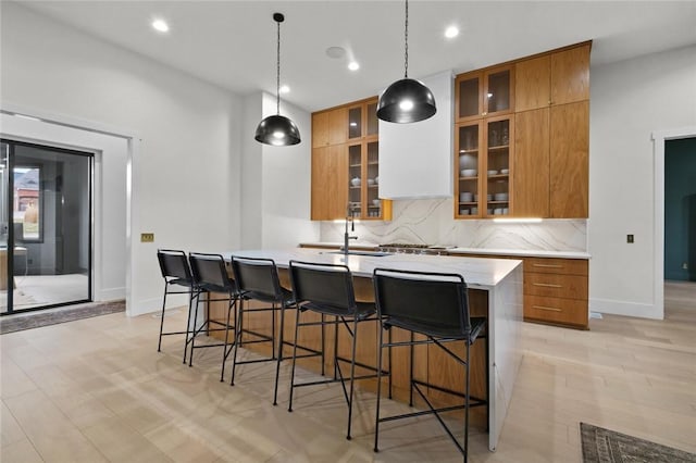 kitchen featuring brown cabinetry, an island with sink, a kitchen breakfast bar, a sink, and backsplash