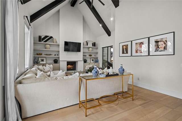 living area featuring high vaulted ceiling, beamed ceiling, a lit fireplace, and wood finished floors