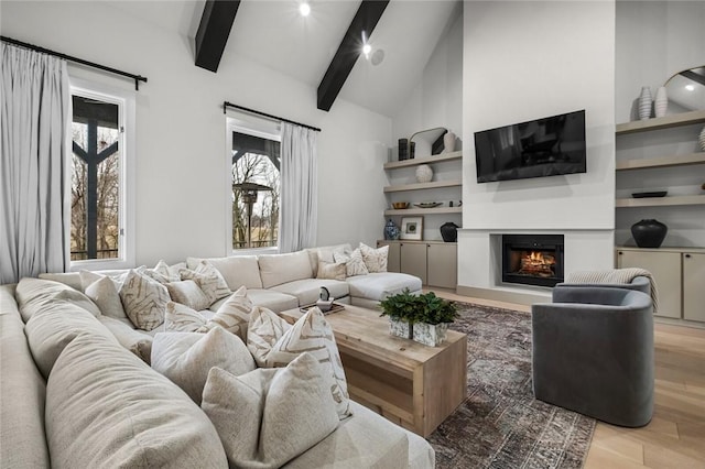 living area with light wood-type flooring, a glass covered fireplace, beamed ceiling, and high vaulted ceiling