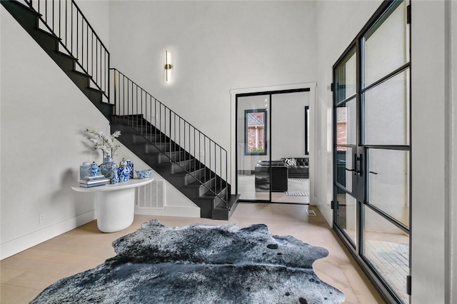 foyer with wood finished floors, visible vents, a towering ceiling, baseboards, and stairway