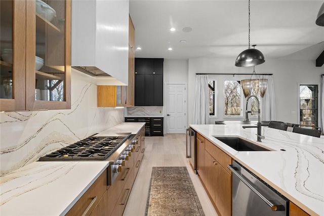 kitchen with tasteful backsplash, modern cabinets, appliances with stainless steel finishes, light stone counters, and a sink