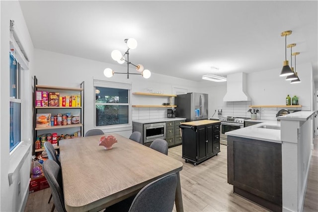 kitchen with light wood finished floors, custom exhaust hood, light countertops, appliances with stainless steel finishes, and a sink