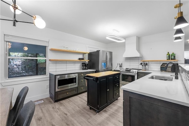 kitchen with stainless steel appliances, dark cabinetry, premium range hood, open shelves, and a sink