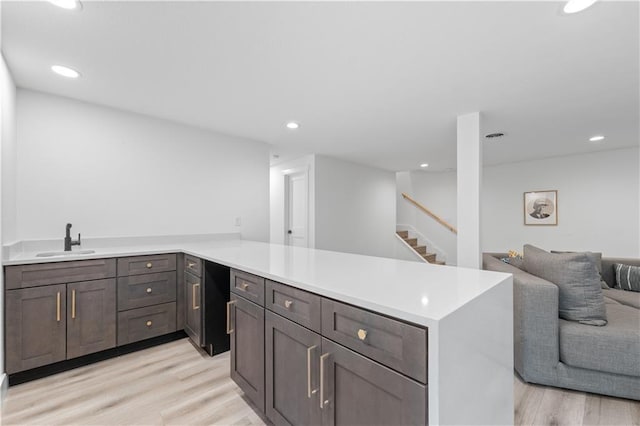 kitchen featuring light wood-style flooring, open floor plan, a peninsula, a sink, and recessed lighting