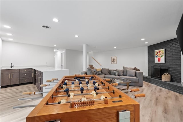 game room featuring recessed lighting, a sink, visible vents, light wood-type flooring, and a brick fireplace