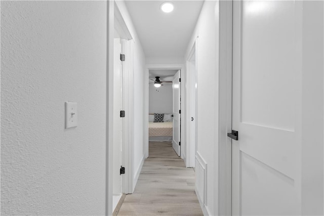 corridor with a textured wall and light wood finished floors