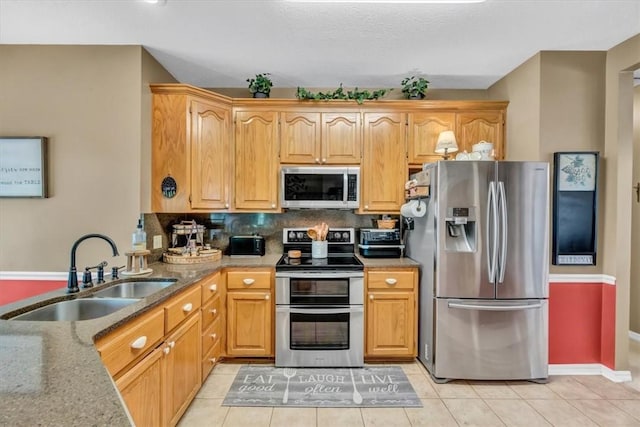 kitchen featuring light tile patterned floors, tasteful backsplash, appliances with stainless steel finishes, a sink, and light stone countertops