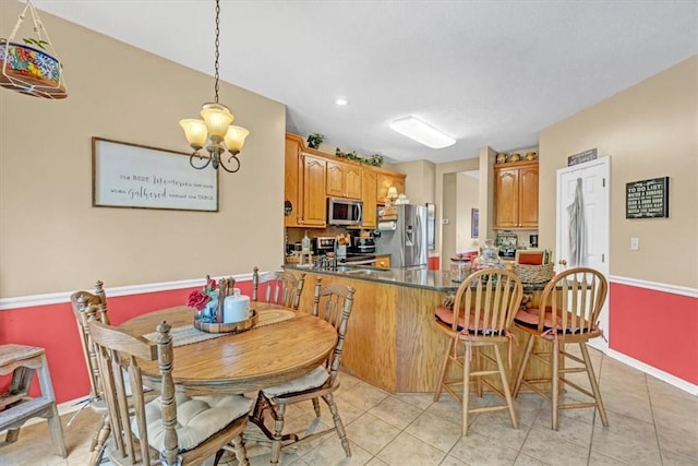 kitchen featuring light tile patterned floors, a breakfast bar area, a peninsula, appliances with stainless steel finishes, and dark countertops