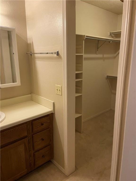 bathroom with a spacious closet, baseboards, a textured ceiling, and vanity