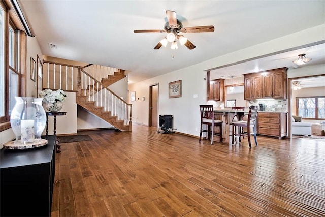 living room with stairs, dark wood-style flooring, a wood stove, and a ceiling fan