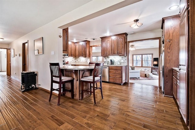 interior space featuring dark wood finished floors, a breakfast bar, a peninsula, stainless steel dishwasher, and backsplash