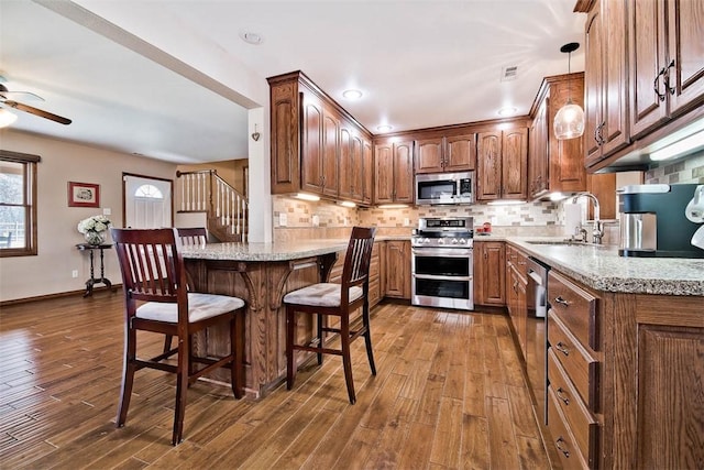 kitchen with appliances with stainless steel finishes, a breakfast bar, dark wood-type flooring, a sink, and backsplash