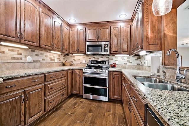 kitchen with light stone counters, stainless steel appliances, a sink, decorative backsplash, and dark wood-style floors