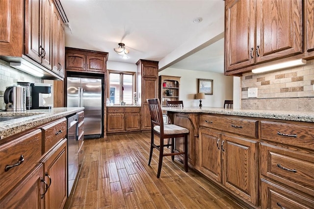 kitchen featuring a breakfast bar, appliances with stainless steel finishes, decorative backsplash, light stone countertops, and dark wood finished floors