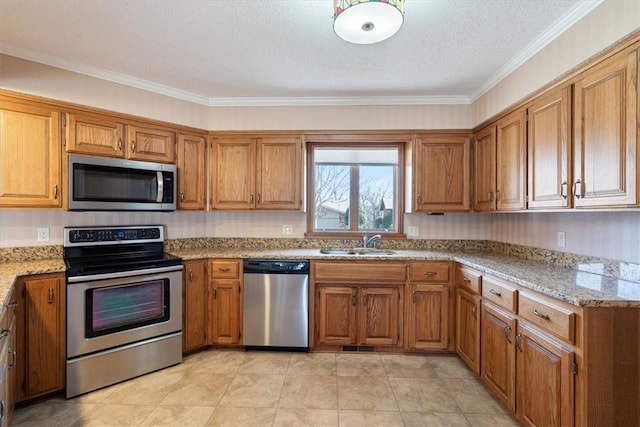 kitchen featuring brown cabinets, appliances with stainless steel finishes, a sink, a textured ceiling, and light stone countertops