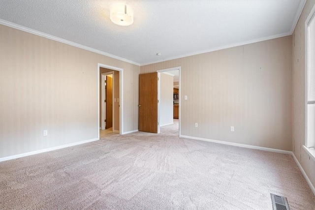 unfurnished room with a textured ceiling, light colored carpet, visible vents, baseboards, and ornamental molding