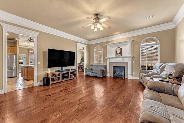 living area featuring a fireplace, visible vents, light wood-style floors, ornamental molding, and a ceiling fan