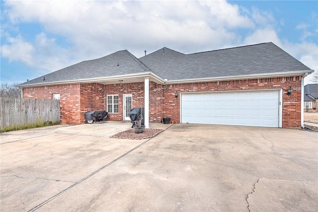 view of front of house with a garage, brick siding, fence, driveway, and roof with shingles