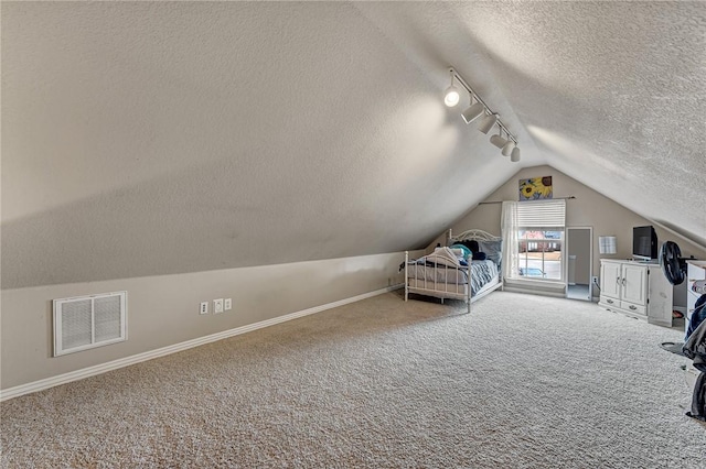 unfurnished bedroom featuring visible vents, carpet flooring, vaulted ceiling, a textured ceiling, and track lighting