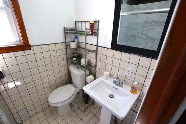 half bathroom featuring toilet, tile patterned flooring, tile walls, and a sink