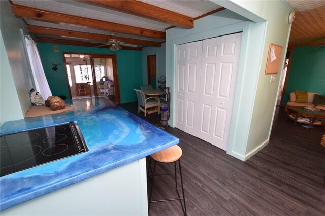 interior space featuring baseboards, dark wood-style floors, ceiling fan, black electric stovetop, and beam ceiling