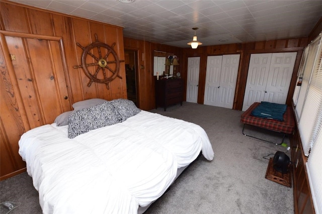 carpeted bedroom with wood walls and multiple closets