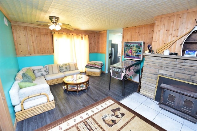 tiled living area with wooden walls, a fireplace, and a ceiling fan