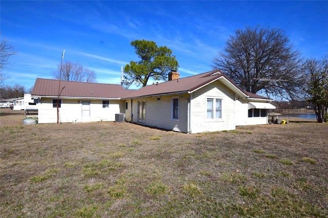 rear view of house with a lawn, metal roof, a chimney, and central AC unit