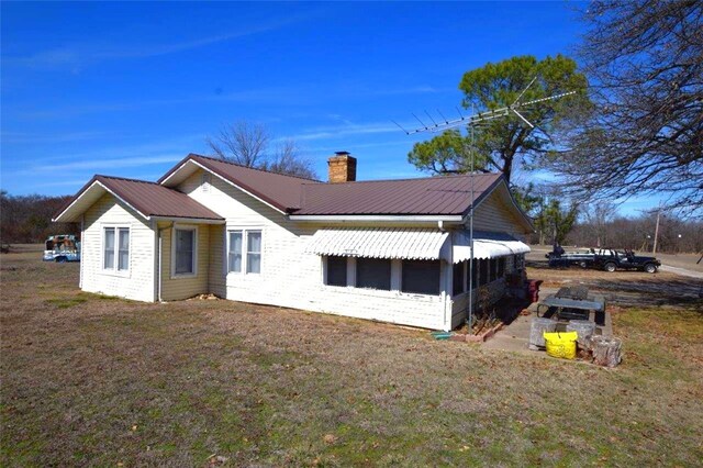 rear view of house featuring a chimney, metal roof, and a lawn