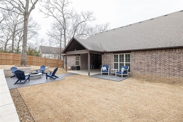 back of house with brick siding, a patio, a shingled roof, an outdoor fire pit, and fence