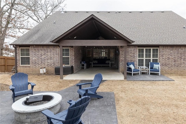 back of house with brick siding, a shingled roof, fence, a patio area, and an outdoor living space with a fire pit