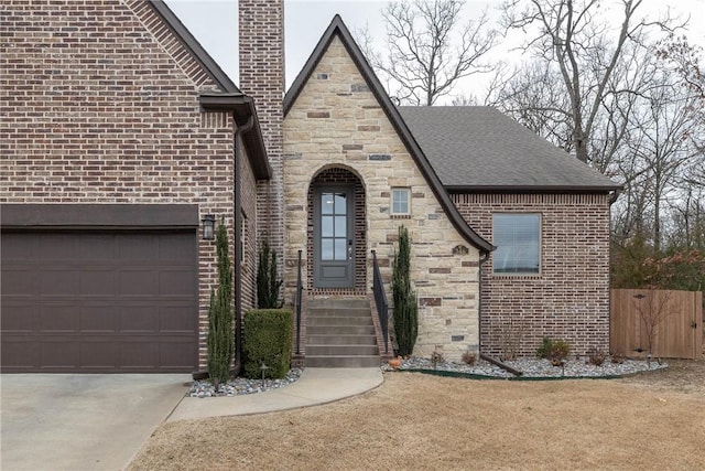 english style home with a chimney, fence, a garage, stone siding, and driveway