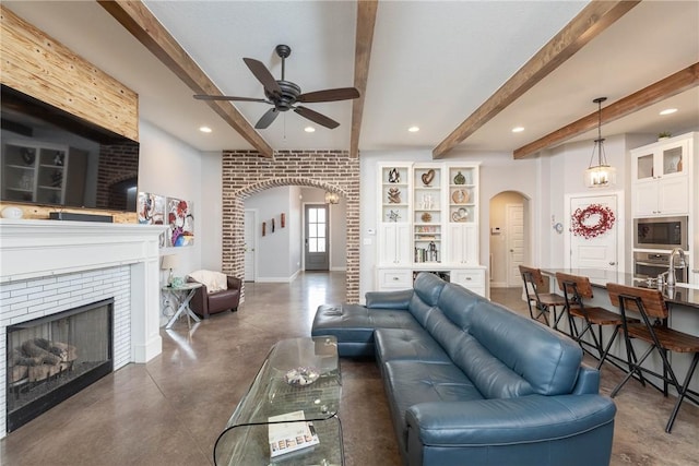 living area featuring finished concrete flooring, a fireplace, arched walkways, and beamed ceiling