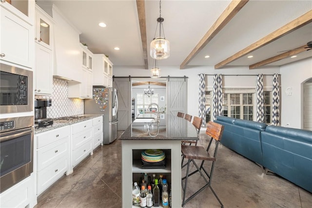 kitchen featuring a breakfast bar, stainless steel appliances, backsplash, a barn door, and dark stone counters