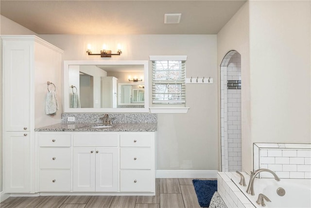 bathroom featuring vanity, visible vents, baseboards, tiled shower, and a bath