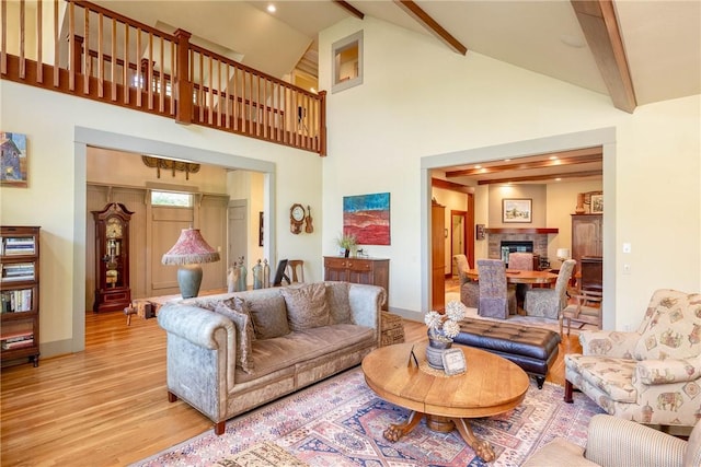 living room featuring baseboards, a glass covered fireplace, light wood-type flooring, high vaulted ceiling, and beam ceiling