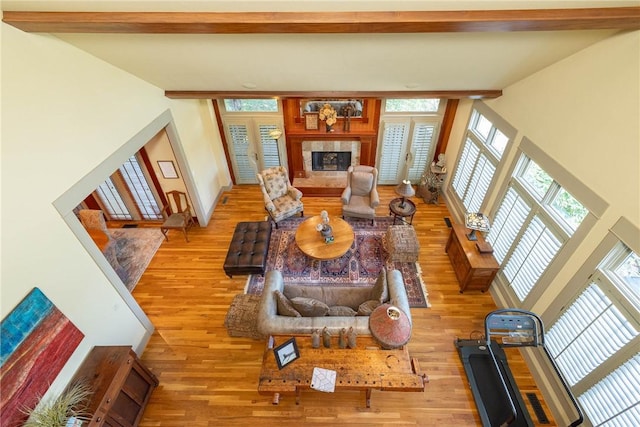 living area featuring a wealth of natural light, a tile fireplace, beamed ceiling, and light wood-style flooring