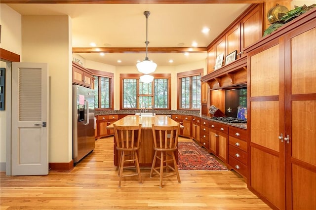 kitchen featuring light wood finished floors, a kitchen bar, appliances with stainless steel finishes, and brown cabinetry