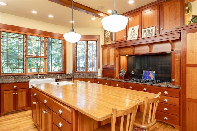 kitchen with brown cabinetry, a center island, light stone countertops, gas stovetop, and a sink