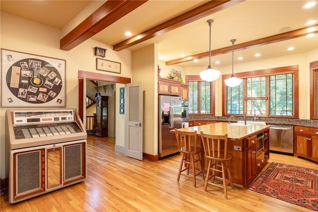 kitchen with brown cabinets, light wood finished floors, a breakfast bar area, appliances with stainless steel finishes, and beamed ceiling