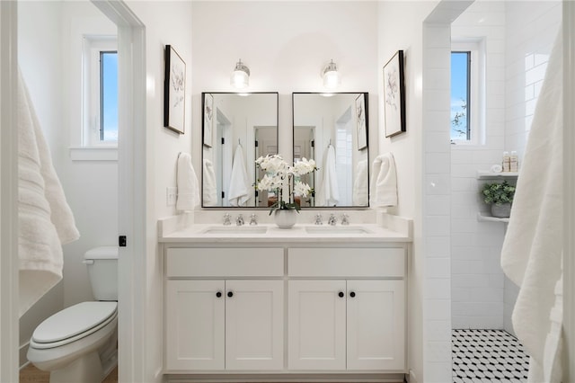 bathroom featuring a tile shower, double vanity, a sink, and toilet