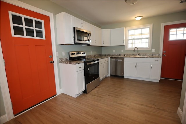 kitchen featuring stainless steel appliances, dark wood-style flooring, a sink, white cabinetry, and dark stone counters