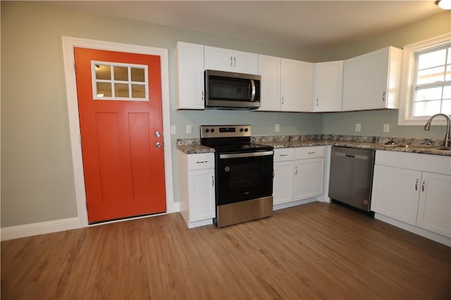 kitchen featuring baseboards, stainless steel appliances, light wood-style floors, white cabinetry, and a sink