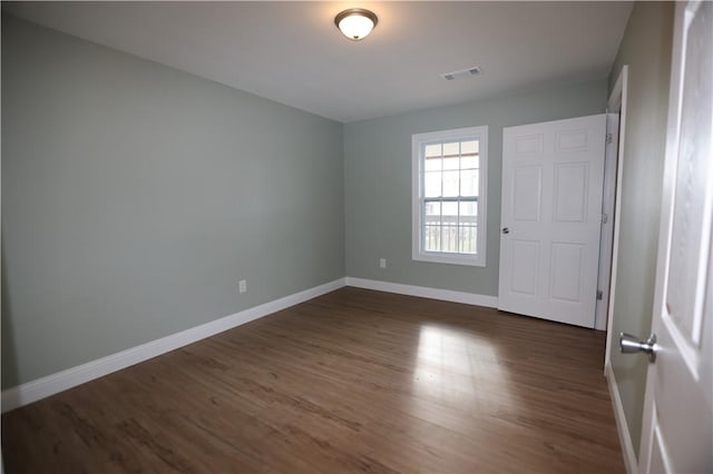 empty room with dark wood-style flooring, visible vents, and baseboards