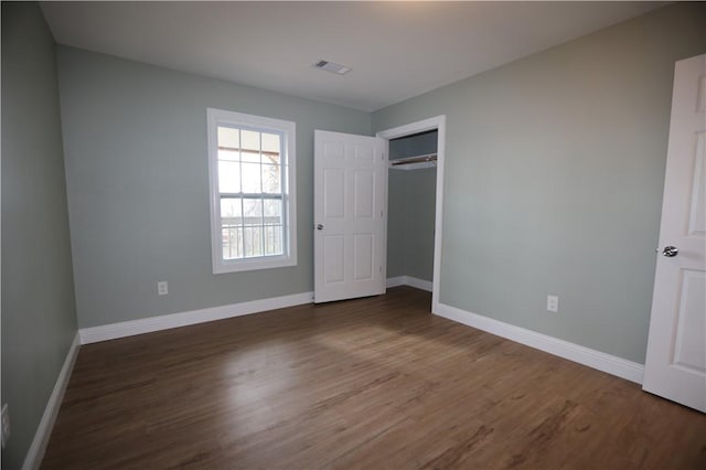 unfurnished bedroom featuring a closet, wood finished floors, visible vents, and baseboards