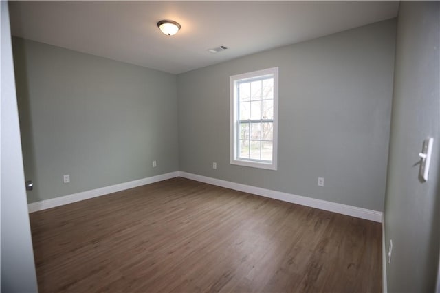 unfurnished room with baseboards, visible vents, and dark wood-type flooring